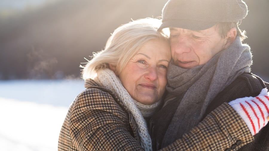 Couple standing outside in the snow with winter clothes on and hugging